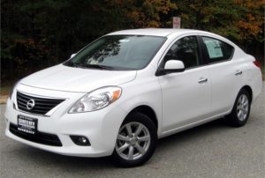 White Nissan sedan parked on a street with trees in background